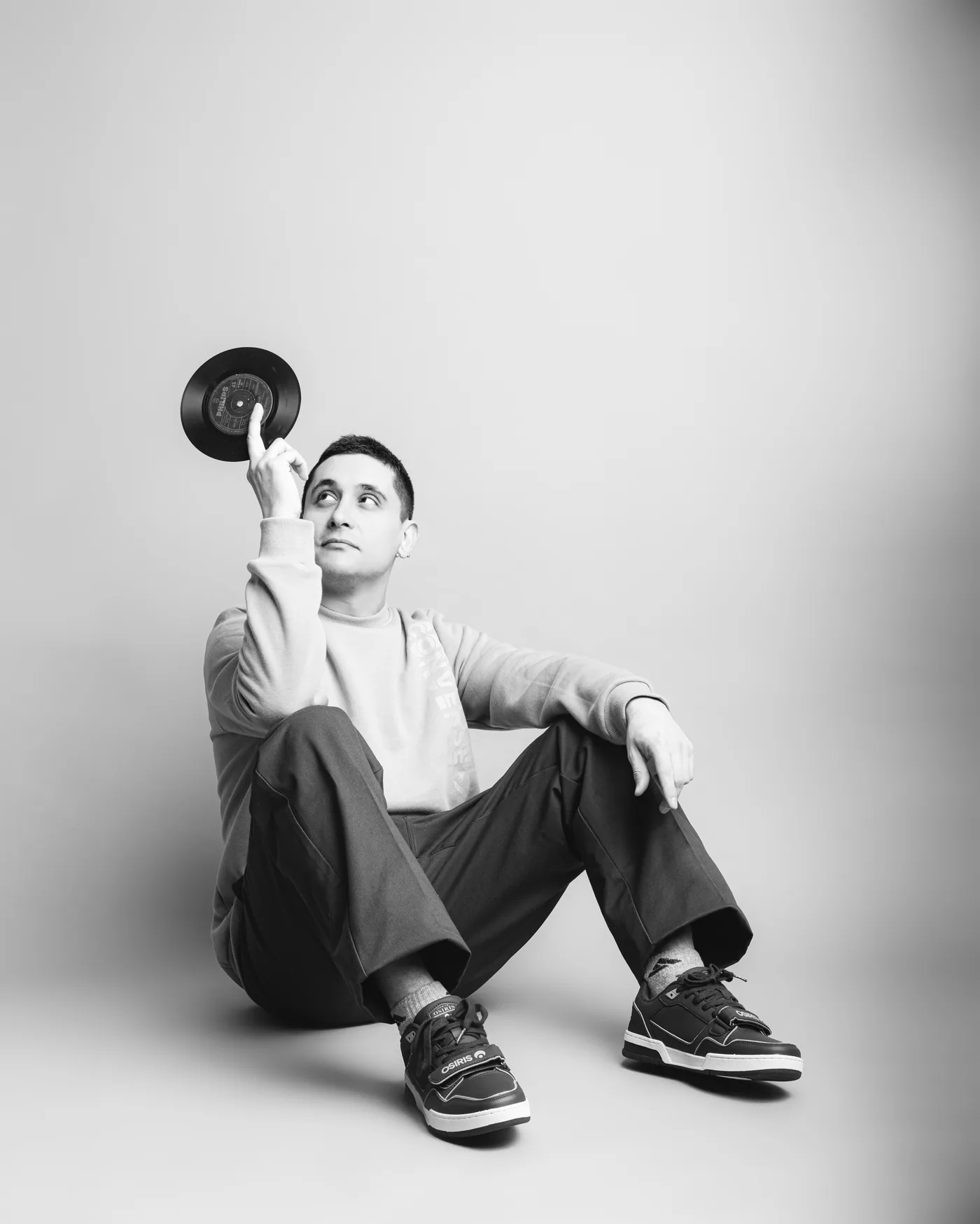 DJ de SeipiesMusic sentado, sosteniendo un vinilo en alto, retrato editorial